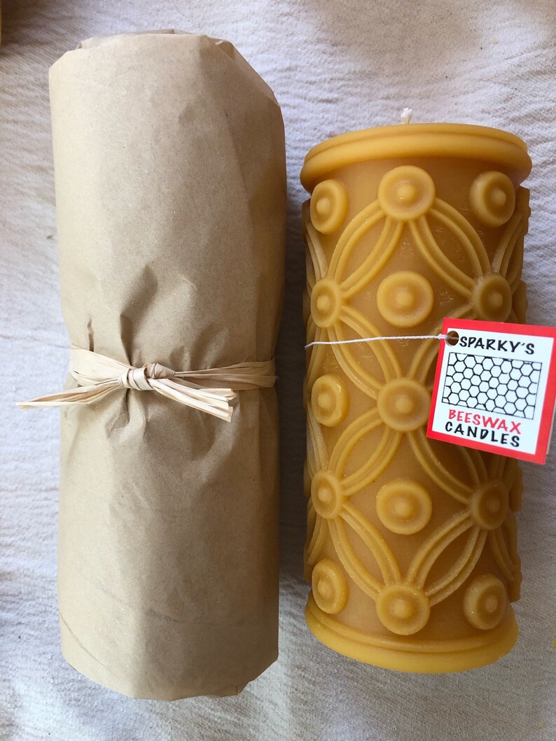 May include: A brown paper wrapped beeswax candle with a decorative pattern and a red label that says "Sparky's Beeswax Candles".