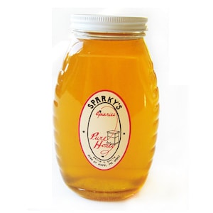May include: A glass jar of honey with a white lid and a label that reads "Sparky's Apiaries Pure Honey Bottled & Packaged by Sparky's Apiaries Hope, MI 49619".