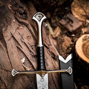 May include: A detailed image of a decorative sword with a silver blade and a black leather-wrapped handle. The hilt and crossguard feature ornate gold-colored accents. The sword rests on a textured wooden surface, with a black sheath visible.