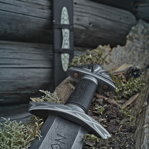 May include: A detailed image of a sword with a patterned blade and a dark wooden handle. The sword is resting on a bed of moss and wood, with its sheath visible in the background. The design includes intricate metalwork.