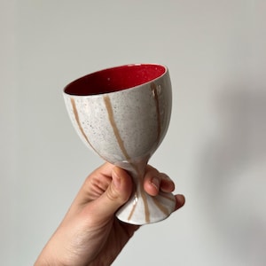 Può includere: Un calice in ceramica fatto a mano con un esterno bianco maculato e un interno rosso vibrante. Il calice presenta gocce di smalto marrone verticali e uno stelo. Questo pezzo unico è perfetto per servire vino o altre bevande.