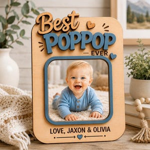 May include: Wooden photo frame with the words "Best Poppop Ever" in brown and blue. The frame holds a photo of a smiling baby. The bottom of the frame reads "Love, Jaxon & Olivia".