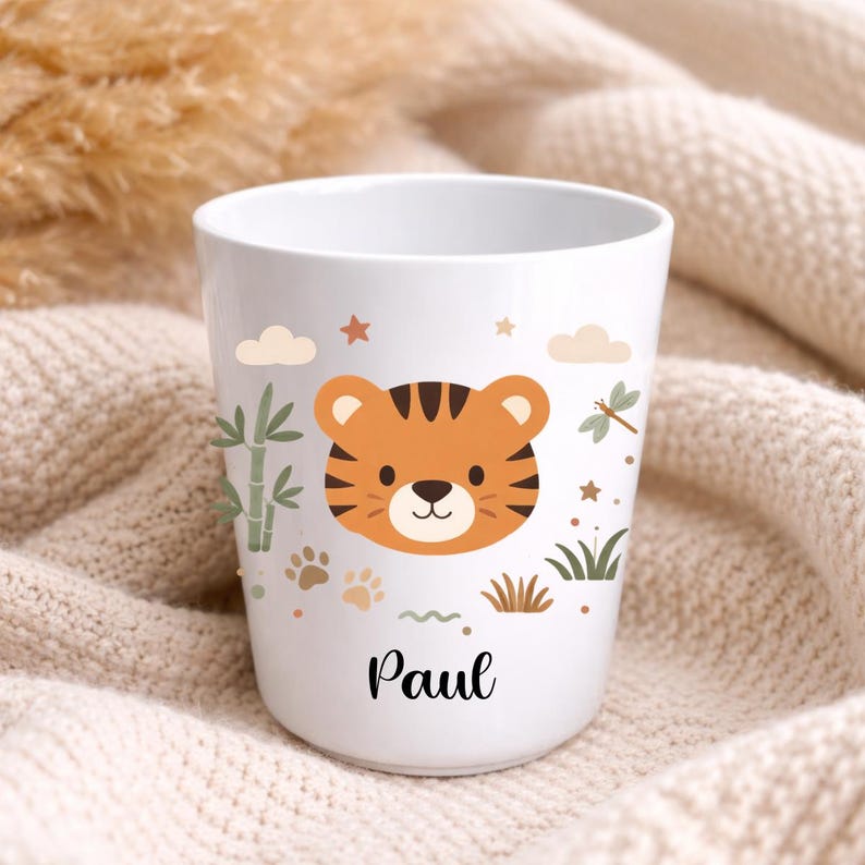 Pu&ograve; includere: Bicchiere in ceramica bianca con un volto di tigre dei cartoni animati a strisce arancioni e nere, decorato con stelle, nuvole e bamb&ugrave;. Il nome "Paul" &egrave; scritto in corsivo nero sotto l'illustrazione della tigre. Un design carino e giocoso.