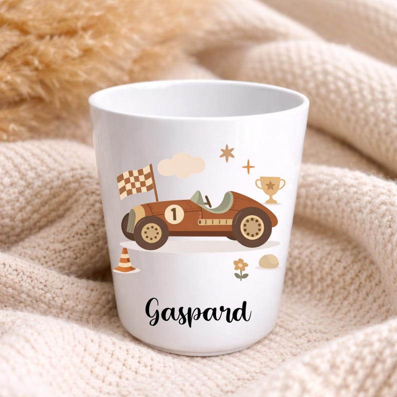 Puede incluir: Taza de cer&aacute;mica blanca con un dise&ntilde;o de coche de carreras marr&oacute;n, una bandera a cuadros y el nombre "Gaspard". La ilustraci&oacute;n incluye un trofeo, una nube, una estrella, una flor y un cono de tr&aacute;fico.