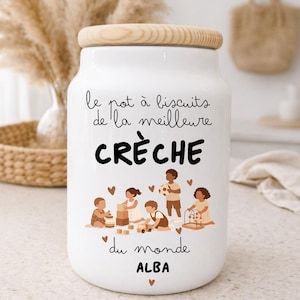 May include: White ceramic cookie jar with a wooden lid. The jar features the text "le pot à biscuits de la meilleure CRÈCHE du monde ALBA" and an illustration of children playing. The jar is designed for storing cookies.