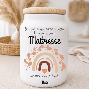 Peut inclure: Pot en céramique blanc avec un couvercle en bois. Le pot porte l'inscription "le pot à gourmandises de ma super Maîtresse" et "merci pour tout Malo" avec un motif arc-en-ciel et cœur. Article décoratif.