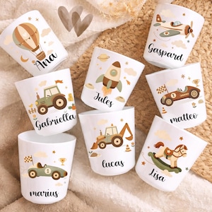 May include: White ceramic cups featuring illustrations of a hot air balloon, airplane, rocket, race car, tractor, and rocking horse. Each cup has a name printed on it: Ana, Gaspard, Jules, Matteo, Gabriella, Lucas, Marius, and Lisa.