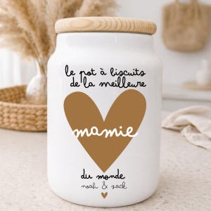 Peut inclure: Pot à biscuits en céramique blanche avec un couvercle en bois. Le pot présente un cœur marron avec le mot "mamie" en écriture blanche. Le texte en français se lit "le pot à biscuits de la meilleure mamie du monde noah & zack."