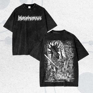 Op de afbeelding: Twee zwarte t-shirts met een verweerde uitstraling. Eén shirt heeft het woord "Blasphemous" in witte, gestileerde letters. Het andere shirt toont een gedetailleerde zwart-wit illustratie van een gevechtsscène met zwaarden en figuren.