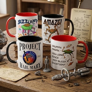 Puede incluir: Cuatro tazas de cerámica con diseños únicos. Una taza tiene "JAZZLAND" con un extraterrestre de dibujos animados, otra dice "AMAZE!" con un robot, una tercera dice "PROJECT HAIL MARY", y la última dice "GRUMPY. ANGRY." con un tema espacial.
