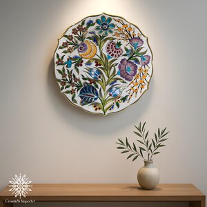 Puede incluir: Un plato decorativo de cer&aacute;mica con un dise&ntilde;o floral. El plato tiene un fondo blanco con flores coloridas en tonos de azul, morado, amarillo y verde. Tiene un borde dorado y est&aacute; montado en una pared.