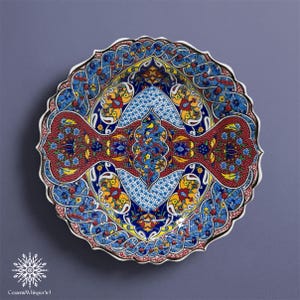 Könnte beinhalten: Ein dekorativer Keramikteller mit gewelltem Rand. Der Teller weist ein lebendiges, kompliziertes Design mit roten, blauen, gelben und weißen Blumenmustern auf. Der Teller hat einen dunklen Rand und den Text "CeramicWhisper Art" unten.