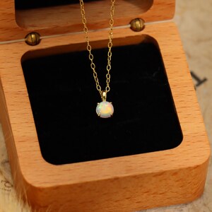 May include: A gold necklace with a round opal pendant rests inside an open wooden jewelry box with a black velvet interior. The opal displays a mix of colors, and the chain is delicate.