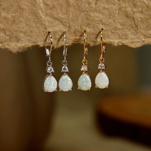 May include: Two pairs of drop earrings featuring pear-shaped white opals with iridescent flecks. One pair is set in silver-toned metal and the other in gold-toned metal. Each earring includes a small clear round stone above the opal and a lever back.