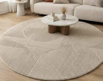 May include: A large, round, beige area rug featuring a textured, geometric pattern of raised lines and circular shapes. The rug is placed on a light-colored wooden floor, showcasing a repeating design of arcs and straight, parallel lines.