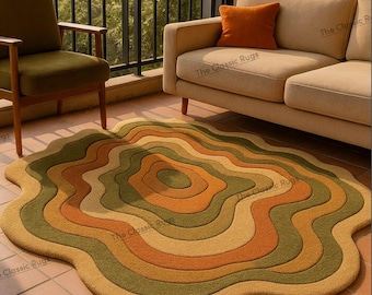 Puede incluir: Una alfombra abstracta con un diseño orgánico en capas. La alfombra presenta bandas concéntricas y onduladas de color en tonos verde oliva, beige y naranja. La alfombra está colocada sobre una superficie de baldosas, con un sofá y una silla en el fondo.