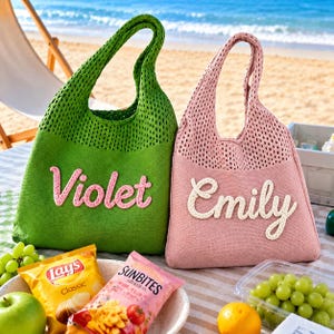 May include: A green knit tote bag with the name Violet in pink yarn and a pink knit tote bag with the name Emily in white yarn. Both bags feature a mesh-style upper section and a solid lower section, designed with a single handle for carrying.