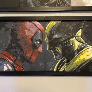 May include: Framed artwork depicting Deadpool and Wolverine in a face-off. Deadpool's mask is red with black detailing, and Wolverine is shown in yellow and black. The background is dark and textured.