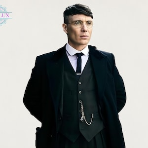 Puede incluir: Un hombre con un traje negro, chaleco y abrigo, con camisa de cuello blanco y corbata oscura. Lleva gafas redondas con montura de alambre y tiene el pelo corto y oscuro. Una cadena de reloj de bolsillo cuelga del chaleco. El texto "OBSILUX" es visible.