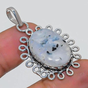 May include: Oval-shaped pendant with a large, iridescent moonstone. The stone has a milky white base with blue and black inclusions. The pendant is set in a silver-colored metal with a decorative, openwork border and a loop for a chain.