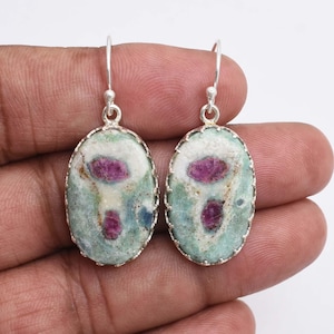Peut inclure: Boucles d'oreilles ovales avec monture argentée. Les boucles présentent une pierre vert clair et blanche avec des inclusions roses. Les boucles sont suspendues à des crochets argentés, présentant un design unique et coloré.