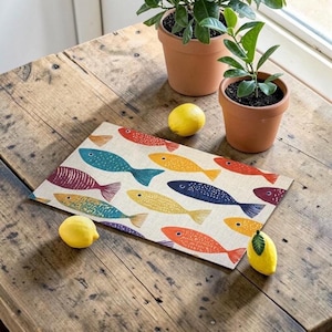 May include: A rectangular placemat featuring a repeating pattern of stylized fish in various colors including red, yellow, blue, and purple on a light beige background. The fish are depicted with simple dotted and lined textures on their bodies.