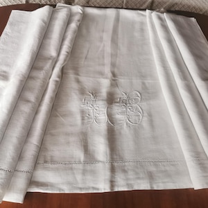 May include: White linen sheet with embroidered floral design. The sheet is folded to display the embroidered detail, with a stitched hem along the bottom. The fabric has a soft, slightly textured appearance.
