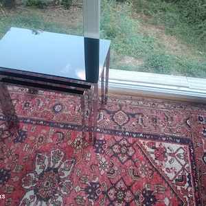 May include: A set of three nesting tables with a black glass top and chrome legs. The tables are placed on a red and brown patterned rug. The image is taken from an elevated angle, showing the tables and rug in detail.