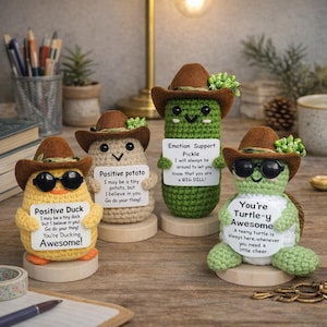 Könnte beinhalten: Vier gehäkelte Figuren: eine gelbe Ente, eine beige Kartoffel, eine grüne Gurke und eine grüne Schildkröte. Jede trägt einen braunen Cowboyhut und eine Sonnenbrille. Das Schild der Ente lautet "Positive Duck". Das Schild der Kartoffel lautet "Positive potato". Das Schild der Gurke lautet "Emotion Support Pickle". Das Schild der Schildkröte lautet "You're Turtle-y Awesome."