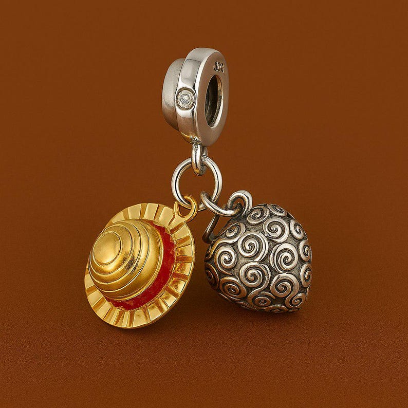 May include: A silver charm with a small diamond, connected to a gold and red hat charm and a silver, swirled design charm. The charms are suspended against a brown background.
