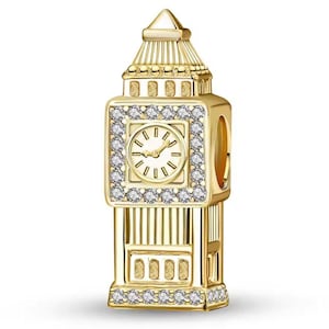 May include: A gold-colored charm in the shape of the Big Ben clock tower. The clock face is visible, surrounded by a square of clear crystals. The charm has a detailed design and is likely for a bracelet or necklace.