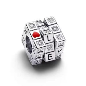 May include: Silver charm with the word "LOVE" spelled out on a cube. The charm has a red heart and clear crystals. The charm is designed to be used with a bracelet or necklace.