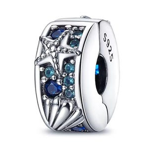 May include: A silver charm with a marine theme. The charm features a starfish and shell design, embellished with blue and teal gemstones. The text "S925" is visible on the side. This charm is designed to be a clip-on style.