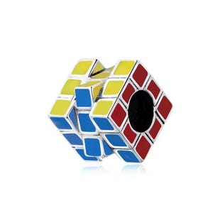 May include: A silver-toned charm in the shape of a Rubik's Cube. The cube features red, yellow, and blue squares. The charm has a hole through the center. The cube is a classic puzzle toy.