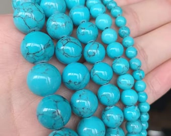 May include: Strands of turquoise beads in varying sizes. The beads are a vibrant blue-green color with dark veining. The beads are round and smooth, and appear to be strung together. The beads are held in a hand.