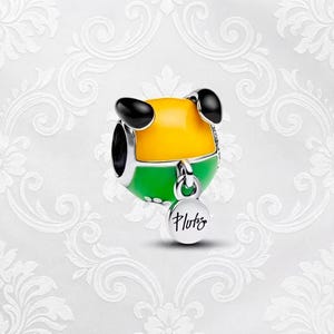 May include: A charm featuring a yellow and green design with black ears, resembling a cartoon dog. The charm has a small, round tag that says "Pluto" in cursive. The charm is likely made of metal and enamel.