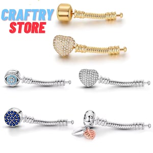 Puede incluir: Una colección de pulseras de abalorios con varios diseños. Los abalorios incluyen una barra dorada, un corazón cubierto de cristales, un ojo con detalles azules, un corazón con cristales y un abalorio con una hoja.