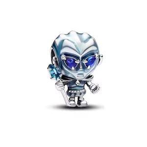 Puede incluir: Un charm plateado que representa una figura alienígena estilizada con una cabeza grande, ojos azules y un bastón con una gema azul. La figura lleva un atuendo azul oscuro y tiene un acabado metálico detallado.