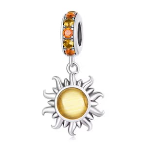 May include: A silver charm with a sun design. The sun has a yellow center and silver rays. The top of the charm has a silver band with orange and yellow gemstones. The charm is suspended from a silver loop.