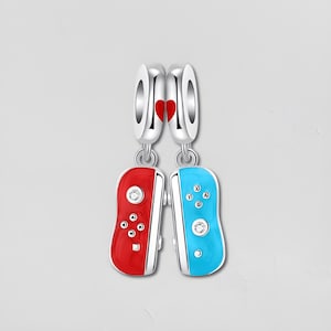 May include: Two silver charms with a red heart and two game controller pendants. One controller is red, the other is blue, each with a silver border and a clear gem. The controllers have buttons and are connected to the silver charm.