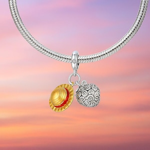 May include: A silver charm bracelet with two pendants. One pendant is a gold and red straw hat, and the other is a silver, patterned fruit. The background is a gradient of pink, orange, and purple.