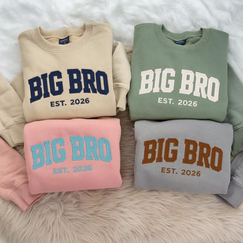 May include: Four crewneck sweatshirts in beige, sage green, light pink, and grey. Each features the embroidered text BIG BRO and EST. 2026 in contrasting colours: navy blue on beige, white on green, light blue on pink, and brown on grey.