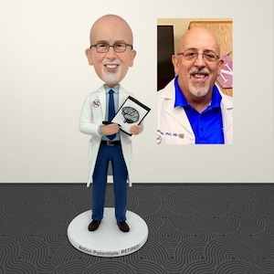 Puede incluir: Una figura cabezona personalizada de una persona calva con perilla blanca, gafas, bata blanca de laboratorio, camisa azul y pantalones azules. La figura sostiene un portapapeles con una ilustración de un cerebro y se apoya en una base con el texto Action Potentials: RETIRED!