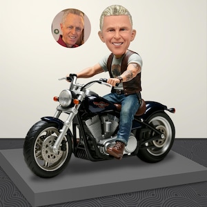 Może przedstawiać: Personalizowana figurka z kiwającą głową przedstawiająca osobę z krótkimi siwymi włosami na ciemnoniebieskim motocyklu. Figurka ma na sobie brązową skórzaną kamizelkę na jasnoszarym t-shircie, niebieskie dżinsy i brązowe buty, z widocznymi tatuażami i zegarkiem.