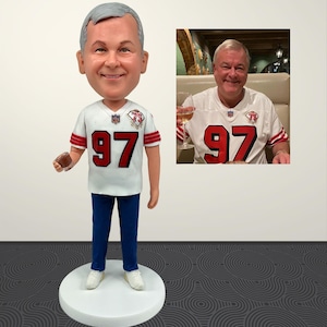 May include: A bobblehead figurine of a man wearing a white jersey with red accents and the number 97. The figurine is on a white base. A smaller image of the man in the same jersey is to the right.