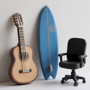 May include: A miniature scene featuring a light brown acoustic guitar, a light blue surfboard with a white fin, and a black office chair. The guitar leans against a white wall, while the surfboard stands upright. The chair is on wheels.