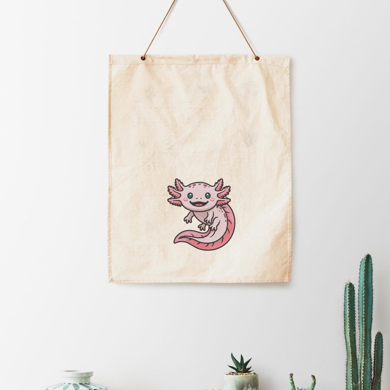 May include: A canvas wall hanging featuring a cartoon axolotl. The axolotl is pink with black outlines, a smiling face, and feathery gills. The background is a cream-colored canvas with a simple hanging cord.