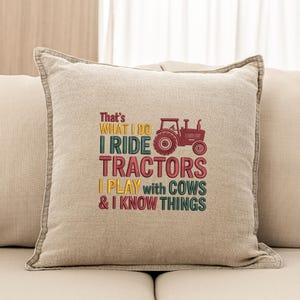 Peut inclure: Un coussin carr&eacute; beige avec un motif brod&eacute;. Le texte dit "That's WHAT I DO I RIDE TRACTORS I PLAY with COWS & I KNOW THINGS" avec un dessin de tracteur rouge.