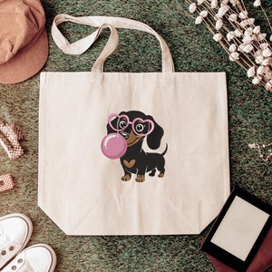 May include: A cream-colored tote bag featuring a cartoon dachshund wearing pink heart-shaped glasses and blowing a pink bubble. The dog has a brown heart on its chest. The bag has a simple design with long handles.