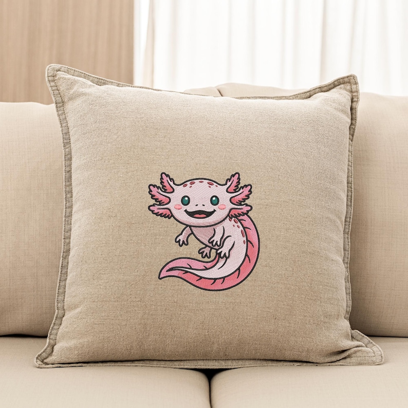 May include: Beige square throw pillow featuring an embroidered axolotl design. The axolotl is pink with black outlines, a smiling face, and feathery gills. The pillow has a neutral color palette and a simple design, suitable for home decor.